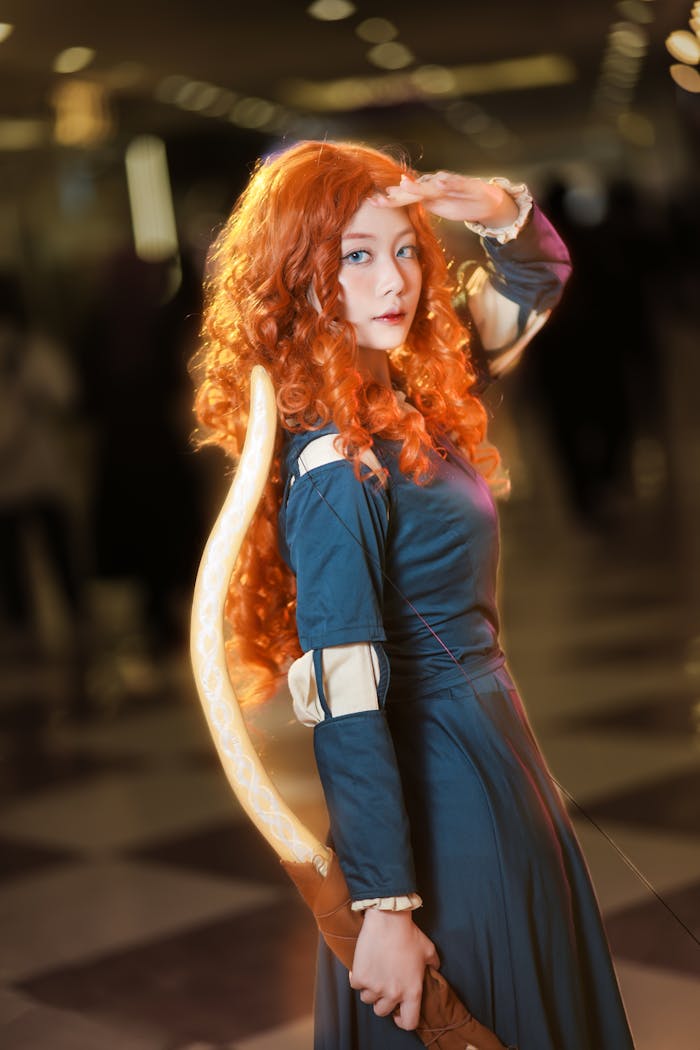 Dynamic cosplay portrayal of a red-haired archer character with bow and costume indoors.